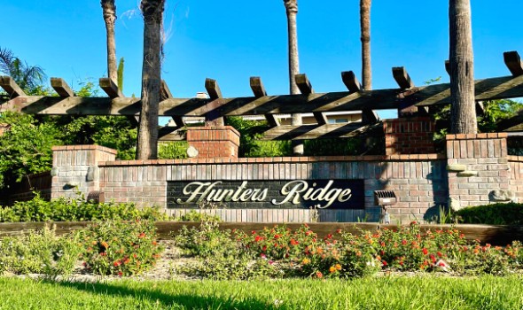 Hunters Ridge Signage attached to a brick wall surrounded by greenery and colorful flowering plants | hunters ridge fontana homes for sale | Alvin Tapia