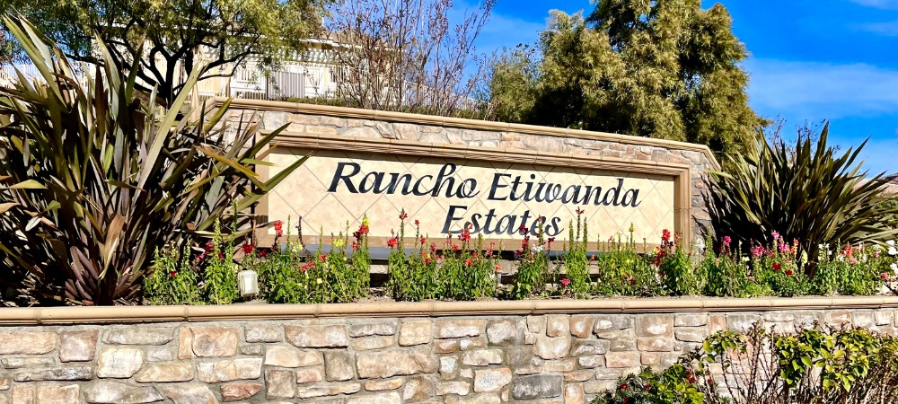 Rancho Etiwanda Estates signage in a stone wall with lots of plant and flowers around-Rancho Etiwanda Estates Homes For Sale-Featured Image | Alvin Tapia